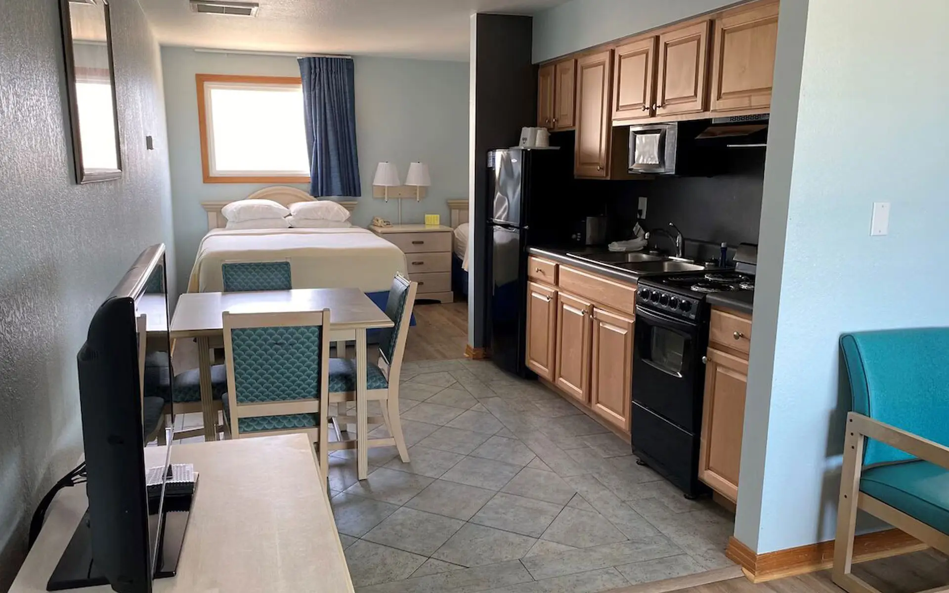 A suite at Mariner Inn & Suites with a bed, a dining table and a full kitchenette with wood cabinets