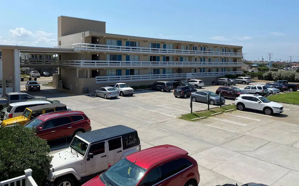Mariner Inn & Suites, a three-storey building with white balcony railings and blue doors, seen from the parking lot with cars parked below