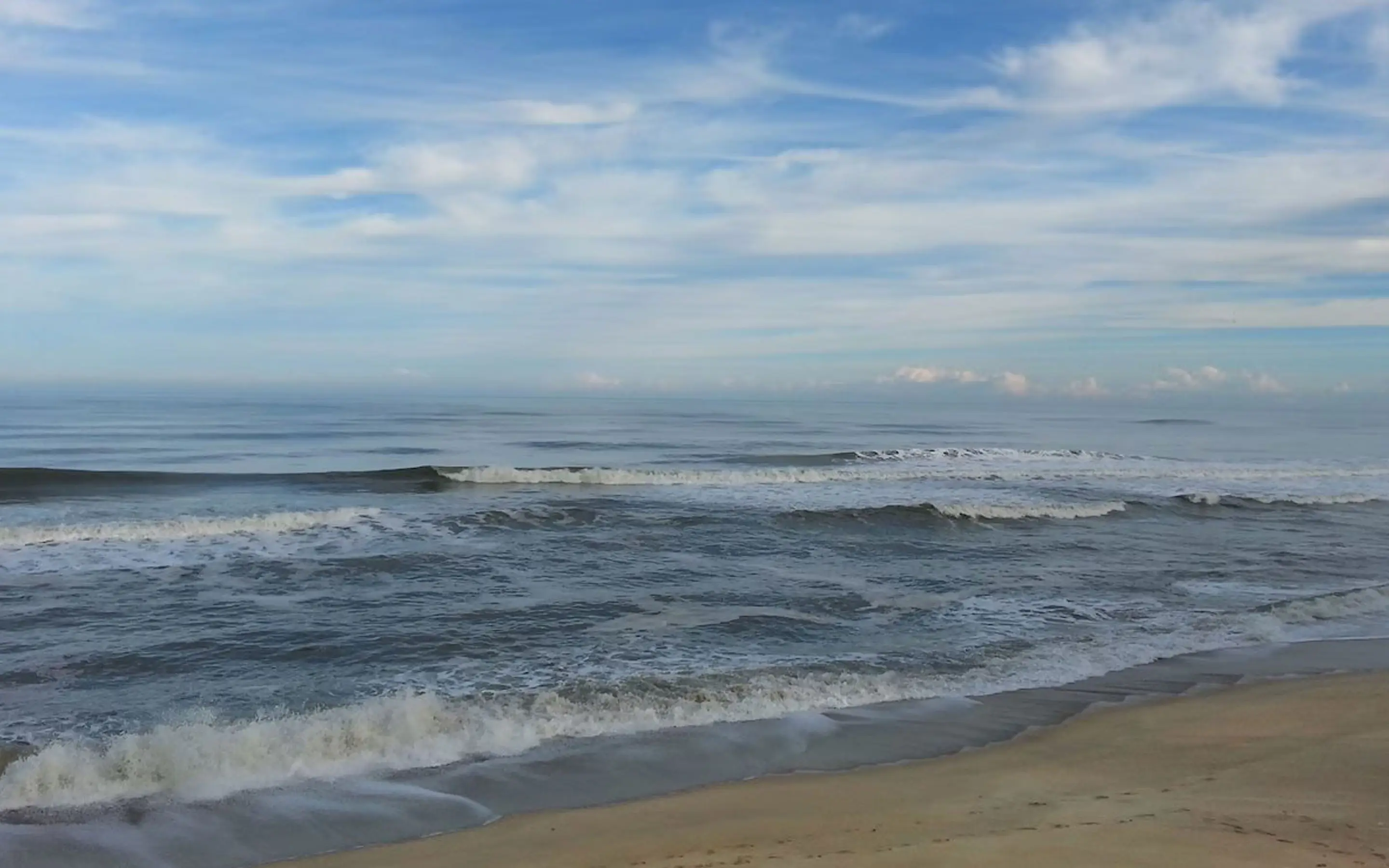 A wide view of the beach and Atlantic Ocean at Kill Devil Hills, North Carolina, with a wooden dune fence in the foreground