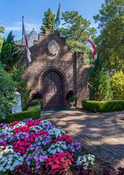 The brick gatehouse entrance to the Elizabethan Gardens, framed by flags and beds of purple, pink and white flowers