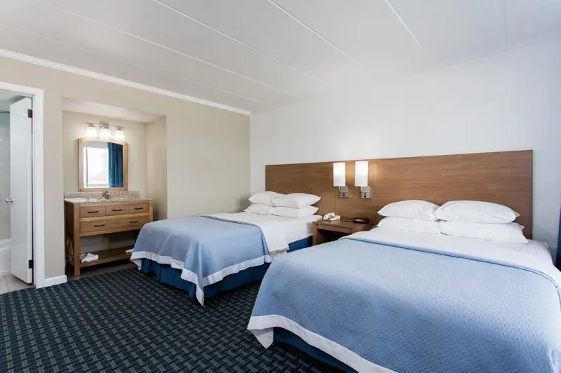 Two beds with blue coverlets in a room at Mariner Inn & Suites, with a wood vanity nook and dark patterned carpet