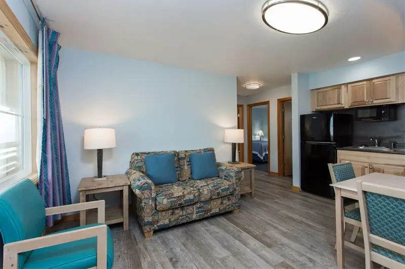 A suite living room at Mariner Inn & Suites with a patterned loveseat, a TV on a wood stand, and a hallway leading to a kitchenette