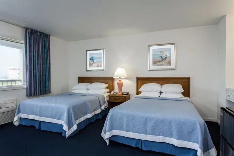 Two beds with blue coverlets at Mariner Inn & Suites, with matching framed beach prints above each headboard