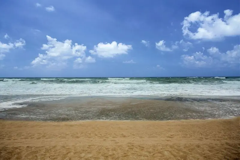 A calm tide pool on the beach at Mariner Inn & Suites, with moderate waves breaking beyond it under a partly cloudy sky