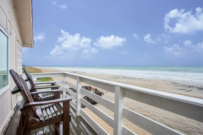 A private balcony at Mariner Inn & Suites with two wooden Adirondack chairs looking out over the sandy beach and the Atlantic Ocean