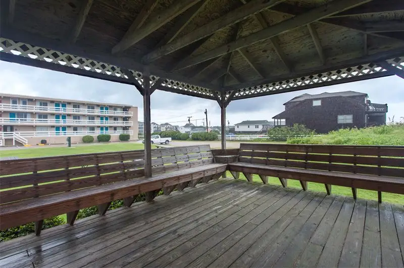 A covered wooden gazebo at Mariner Inn & Suites overlooking a grassy lawn, with a two-storey motel building and parking lot in the background