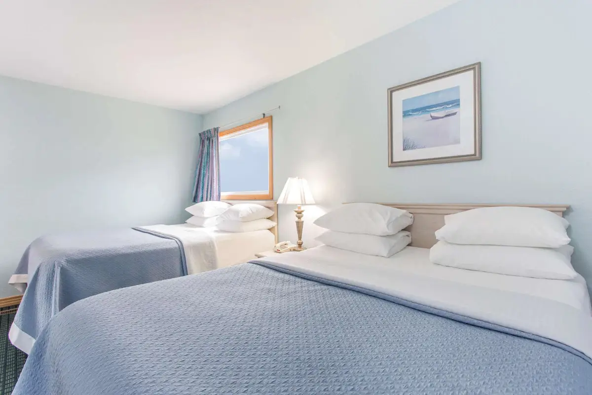 Two beds with pale blue coverlets at Mariner Inn & Suites, with a framed print of a beach chair and umbrella above the headboard