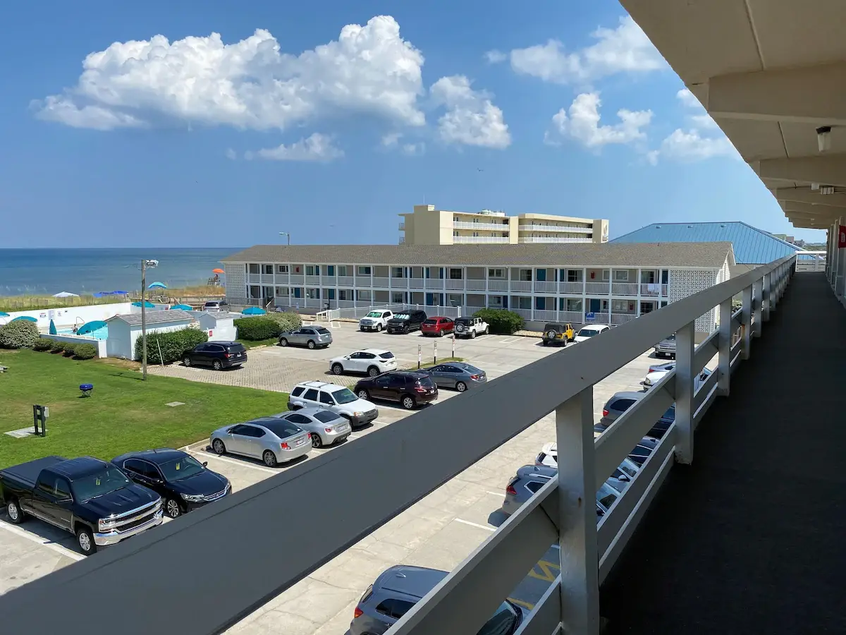 Mariner Inn & Suites seen from an upper-floor walkway, looking down over the outdoor pool to the sand dunes and the Atlantic Ocean