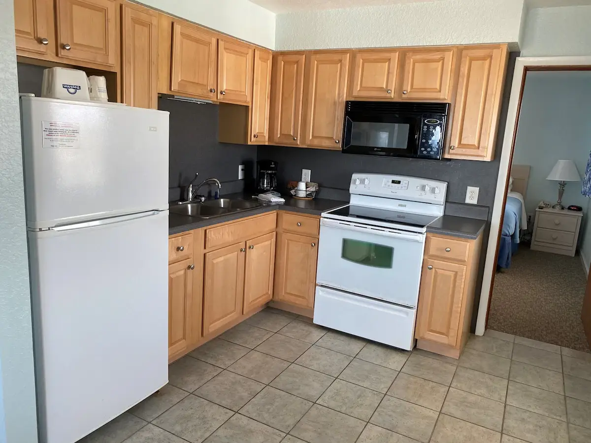 A kitchenette at Mariner Inn & Suites with a white refrigerator, wood cabinets, a black microwave and a white electric range