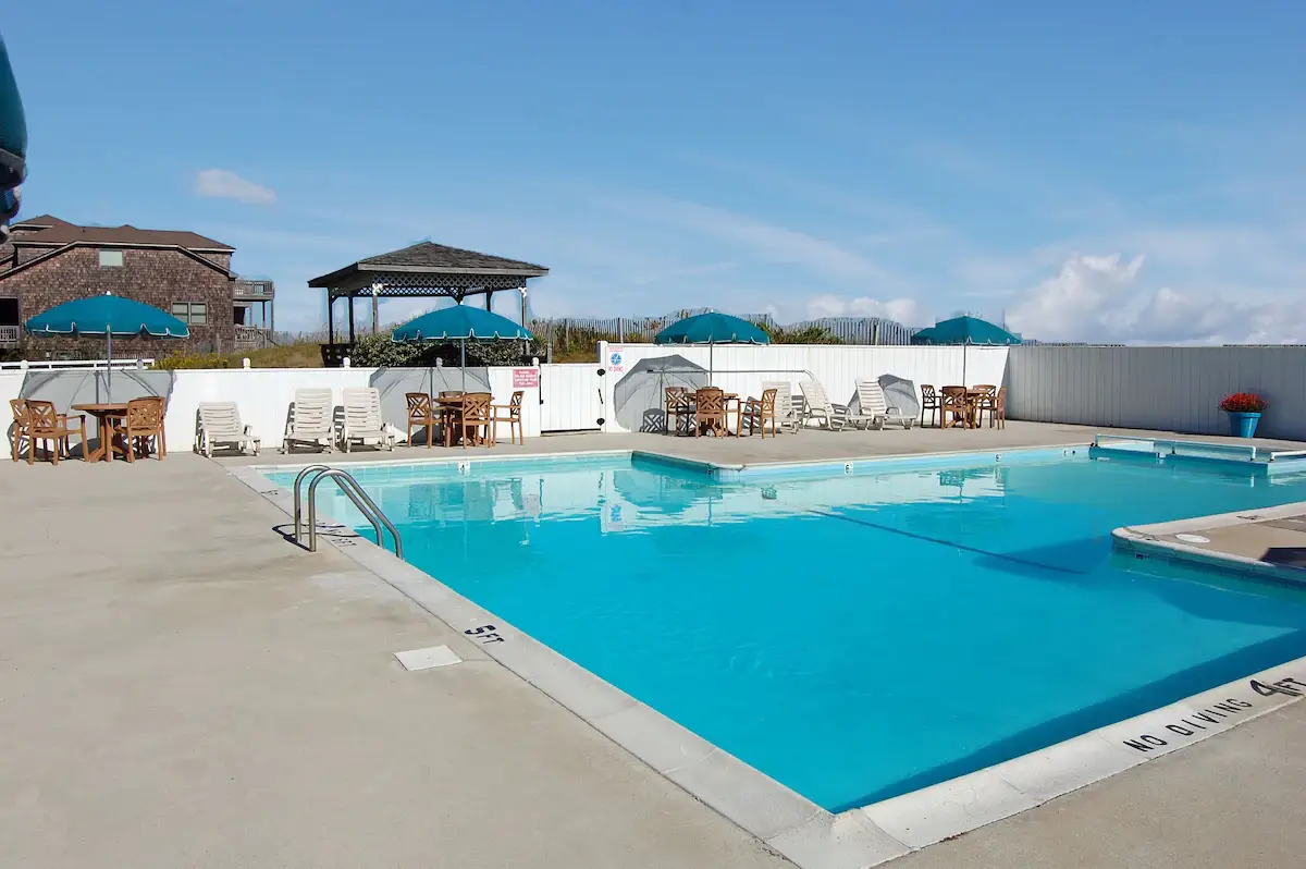 The outdoor pool at Mariner Inn & Suites with teal umbrellas, lounge chairs and a wooden gazebo, with a shingled house in the background