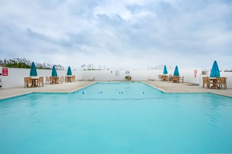 The outdoor pool at Mariner Inn & Suites, with teal umbrellas and chairs on both sides under a cloudy sky