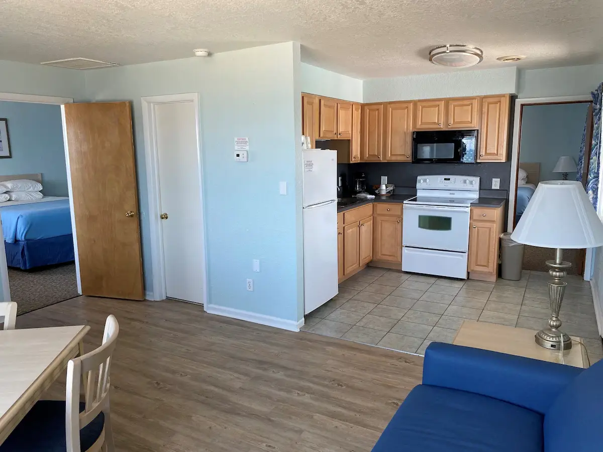 A suite at Mariner Inn & Suites with a bedroom visible through an open doorway on the left and a full kitchen with a white refrigerator on the right