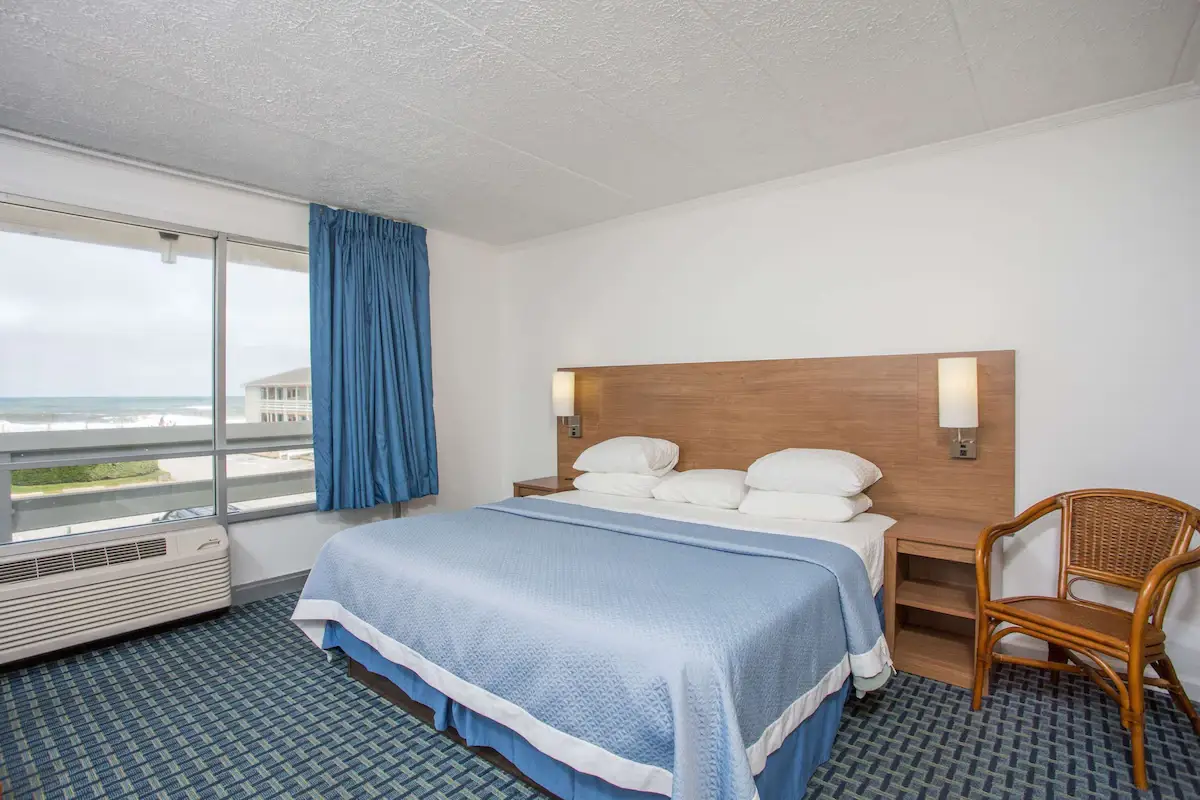 Two beds with blue coverlets at Mariner Inn & Suites, with a dresser and mirror at the left and matching framed beach prints above the headboards