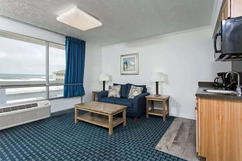 A suite living room at Mariner Inn & Suites with a navy loveseat, a coffee table, an ocean-view window and a kitchenette to the right
