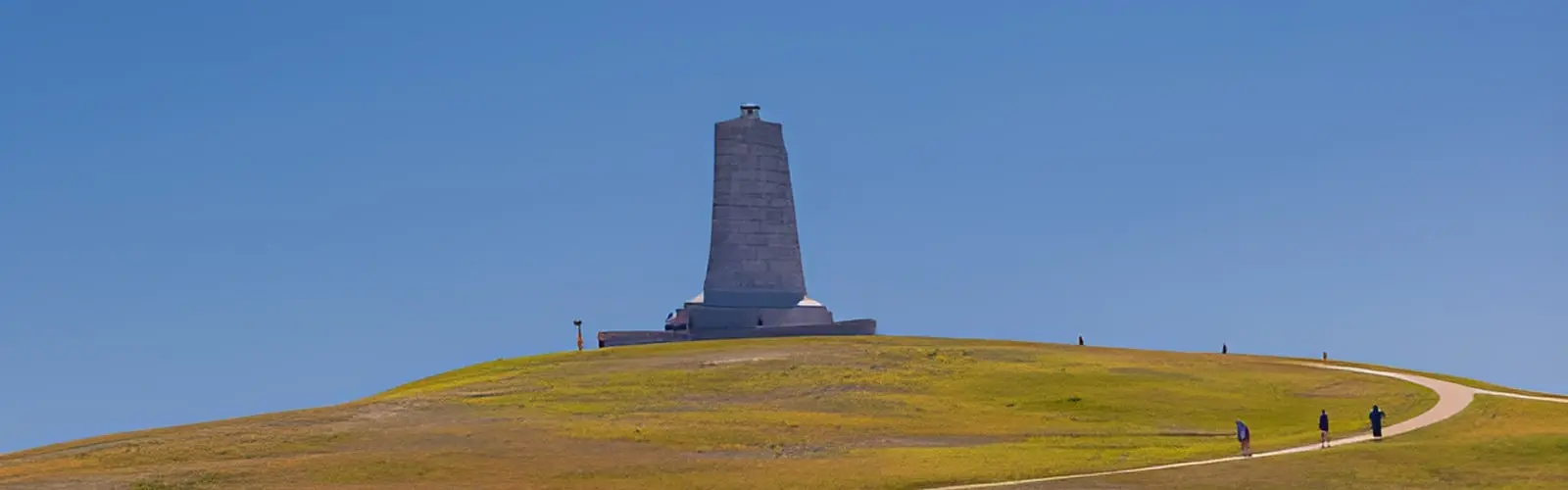 The granite Wright Brothers National Memorial monument on Big Kill Devil Hill under a partly cloudy sky