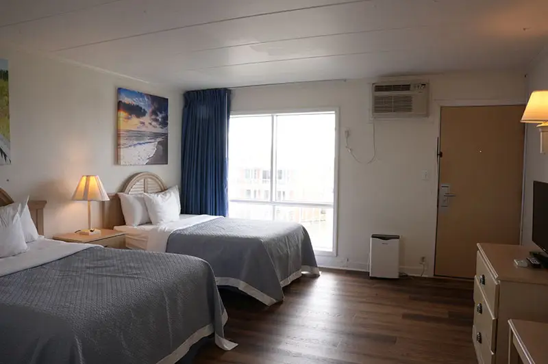Two beds with grey coverlets at Mariner Inn & Suites, with matching sunset-beach canvas prints above the headboards and dark wood-look flooring