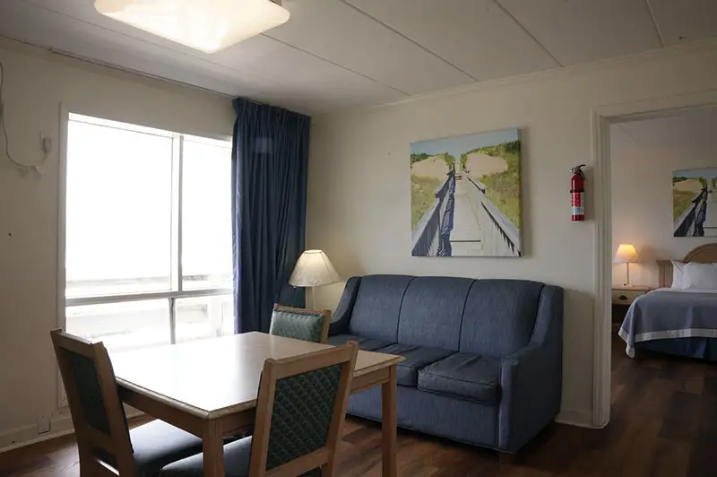 A suite living room at Mariner Inn & Suites with a navy sofa, a dining table, and a canvas print of a boardwalk through the dunes