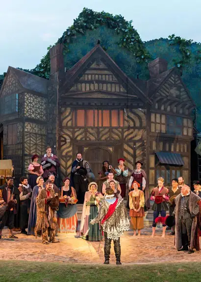 A costumed cast performing on the outdoor stage of The Lost Colony, in front of a Tudor-style set building